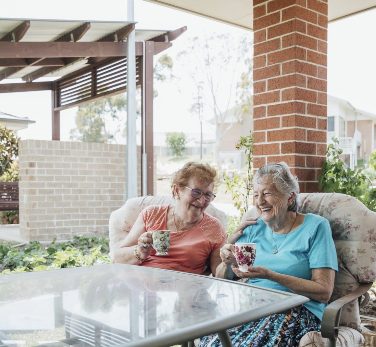 Two elderly friends sitting on their porch enjoying a cup of tea